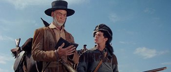 Movie still from “The Alamo” (1960), directed by John Wayne – A man and a man in native american garb looking at a book; Medium shot, Low angle