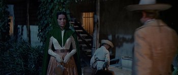 Movie still from “The Alamo” (1960), directed by John Wayne – A woman in a green and white dress standing next to a man in a hat; Medium shot, Low angle