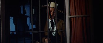 Movie still from “The Alamo” (1960), directed by John Wayne – A man in a suit and hat standing behind bars; Medium shot, Low angle