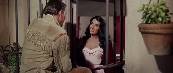 Movie still from “The Alamo” (1960), directed by John Wayne – A woman in a pink dress talking to a man in a cowboy outfit; Medium shot, Over the shoulder angle