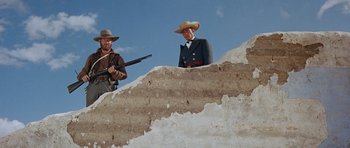 Movie still from “The Alamo” (1960), directed by John Wayne – A man in a cowboy hat standing next to another man in a cowboy outfit; Medium shot, Low angle