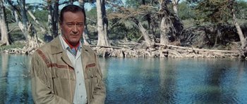 Movie still from “The Alamo” (1960), directed by John Wayne – A man standing in front of a body of water; Medium shot, Over the shoulder angle