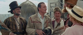 Movie still from “The Alamo” (1960), directed by John Wayne – A man in a native american outfit holding a fur hat; Medium shot, Over the shoulder angle