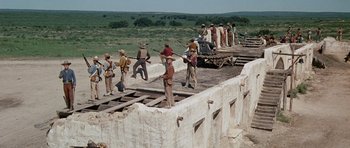 Movie still from “The Alamo” (1960), directed by John Wayne – A group of men standing on top of a train track; Wide shot, Low angle