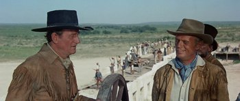 Movie still from “The Alamo” (1960), directed by John Wayne – Two men standing next to each other in front of a fence; Medium shot, Over the shoulder angle