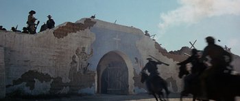 Movie still from “The Alamo” (1960), directed by John Wayne – A man riding a horse in front of a church; Wide shot, Low angle
