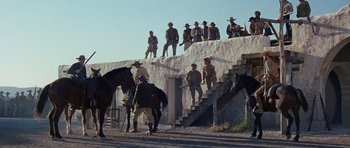 Movie still from “The Alamo” (1960), directed by John Wayne – A group of men standing on top of a set of stairs; Wide shot, Low angle