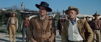 Movie still from “The Alamo” (1960), directed by John Wayne – A man in a cowboy outfit and a man in a cowboy hat; Medium shot, Low angle