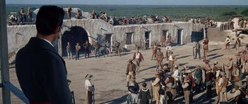 Movie still from “The Alamo” (1960), directed by John Wayne – A group of people standing around a building; Extreme Wide shot, High angle