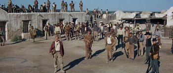 Movie still from “The Alamo” (1960), directed by John Wayne – A group of men standing next to each other on a dirt field; Wide shot, Low angle