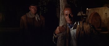 Movie still from “The Alamo” (1960), directed by John Wayne – A man leaning against a tree in a dark forest; Medium shot, Low angle
