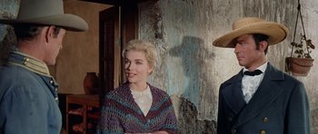 Movie still from “The Alamo” (1960), directed by John Wayne – A woman wearing a purple sweater standing in front of a wall; Close Up shot, Low angle