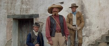 Movie still from “The Alamo” (1960), directed by John Wayne – A group of men standing next to each other holding guns; Medium shot, Low angle