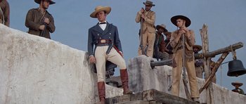 Movie still from “The Alamo” (1960), directed by John Wayne – A group of men standing next to each other on top of a wall; Medium shot, Low angle