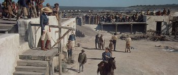 Movie still from “The Alamo” (1960), directed by John Wayne – A group of men standing around a dirt field; Extreme Wide shot, High angle