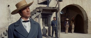 Movie still from “The Alamo” (1960), directed by John Wayne – A man in a cowboy hat standing in front of a building; Medium shot, Low angle
