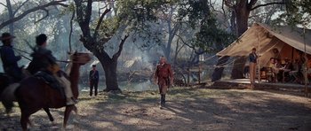 Movie still from “The Alamo” (1960), directed by John Wayne – A man walking in the dirt near a tree; Wide shot, Low angle