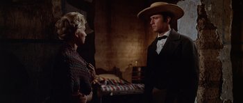 Movie still from “The Alamo” (1960), directed by John Wayne – A man and a woman standing next to each other in a room; Medium shot, Low angle