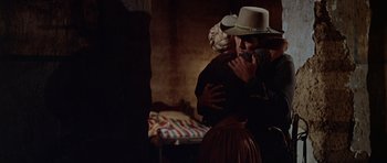 Movie still from “The Alamo” (1960), directed by John Wayne – A man and a woman embracing in a dark room; Medium shot, Over the shoulder angle