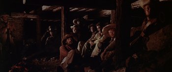 Movie still from “The Alamo” (1960), directed by John Wayne – A group of men sitting on the ground in a barn; Wide shot, Low angle