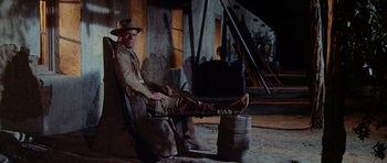 Movie still from “The Alamo” (1960), directed by John Wayne – A man sitting on a chair next to a wooden barrel; Wide shot, Low angle