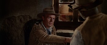 Movie still from “The Alamo” (1960), directed by John Wayne – A man wearing a cowboy hat sitting in front of a window; Medium shot, Over the shoulder angle