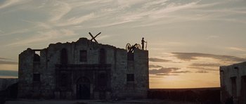 Movie still from “The Alamo” (1960), directed by John Wayne – A man standing on top of an old stone building; Extreme Wide shot, Low angle