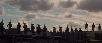 Movie still from “The Alamo” (1960), directed by John Wayne – A group of men in hats are standing on a fence; Extreme Wide shot, Low angle