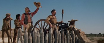 Movie still from “The Alamo” (1960), directed by John Wayne – A group of men standing next to each other near a wooden fence; Wide shot, Low angle