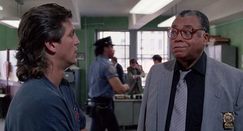 Movie still from “The Ambulance” (1990), directed by Larry Cohen – Two men are talking in an office setting; Medium shot, Over the shoulder angle