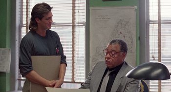 Movie still from “The Ambulance” (1990), directed by Larry Cohen – A man in a suit sitting at a desk talking to another man; Medium shot, Over the shoulder angle
