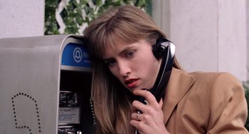 Movie still from “The Ambulance” (1990), directed by Larry Cohen – A woman talking on a payphone while wearing a brown jacket; Close Up shot, High angle