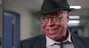 Movie still from “The Ambulance” (1990), directed by Larry Cohen – An older man in a suit and hat smiling; Close Up shot, Over the shoulder angle