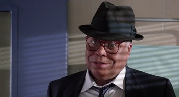 Movie still from “The Ambulance” (1990), directed by Larry Cohen – An older man wearing a hat and glasses; Close Up shot, Over the shoulder angle