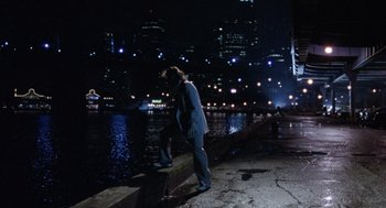 Movie still from “The Ambulance” (1990), directed by Larry Cohen – A woman standing on a ledge near a body of water at night; Extreme Wide shot, High angle