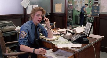 Movie still from “The Ambulance” (1990), directed by Larry Cohen – A police officer sitting at a desk talking on the phone; Medium shot, Over the shoulder angle