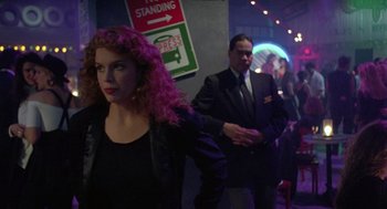 Movie still from “The Ambulance” (1990), directed by Larry Cohen – A woman with pink curly hair standing next to a man in a suit; Medium shot, Over the shoulder angle