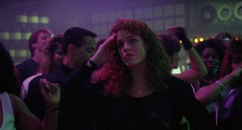 Movie still from “The Ambulance” (1990), directed by Larry Cohen – A woman saluting in a crowd of people at a party; Close Up shot, Over the shoulder angle