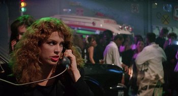 Movie still from “The Ambulance” (1990), directed by Larry Cohen – A woman talking on a phone in front of a group of people; Close Up shot, Low angle