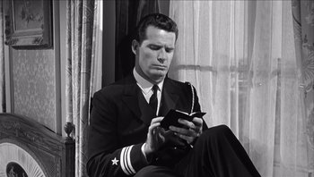 Movie still from “The Americanization of Emily” (1964), directed by Arthur Hiller – A black and white photo of a man in a suit and tie looking at his cell phone; Medium shot, Low angle