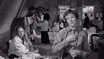 Movie still from “The Americanization of Emily” (1964), directed by Arthur Hiller – A black - and - white photo of a woman tying a neck tie; Medium shot, Over the shoulder angle