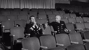 Movie still from “The Americanization of Emily” (1964), directed by Arthur Hiller – Two men sitting in chairs in a theater; Wide shot, High angle