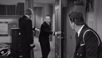 Movie still from “The Americanization of Emily” (1964), directed by Arthur Hiller – A man in a suit and tie standing in front of two other men; Medium shot, Over the shoulder angle