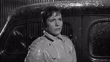 Movie still from “The Americanization of Emily” (1964), directed by Arthur Hiller – Black and white photograph of a woman in a raincoat in the rain; Close Up shot, High angle