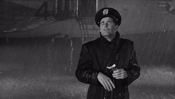 Movie still from “The Americanization of Emily” (1964), directed by Arthur Hiller – A black and white photo of a man in a rain storm; Medium shot, Low angle