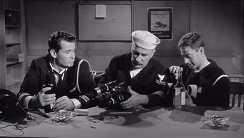 Movie still from “The Americanization of Emily” (1964), directed by Arthur Hiller – A group of men sitting at a table with a bottle of beer; Medium shot, High angle