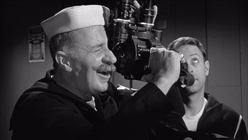 Movie still from “The Americanization of Emily” (1964), directed by Arthur Hiller – An older man holding a camera up to his face; Medium shot, Low angle