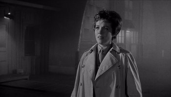 Movie still from “The Americanization of Emily” (1964), directed by Arthur Hiller – A woman wearing a trench coat standing in a dimly - lit room; Medium shot, Low angle