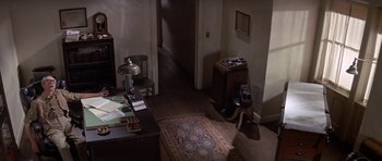 Movie still from “The Andromeda Strain” (1971), directed by Robert Wise – A room with a rug , a desk , a lamp , and a suitcase; Wide shot, High angle
