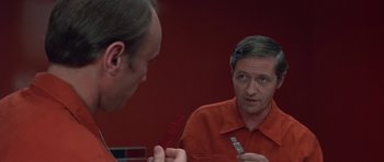 Movie still from “The Andromeda Strain” (1971), directed by Robert Wise – A man looking at himself in the mirror in front of a red wall; Close Up shot, Over the shoulder angle